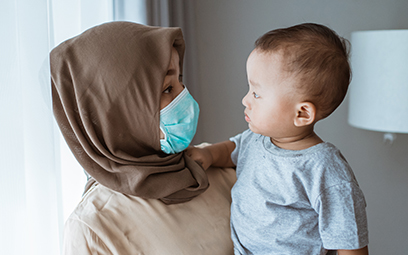 A mother holding her young child and wearing a protective mask to help prevent the spread of COVID-19
