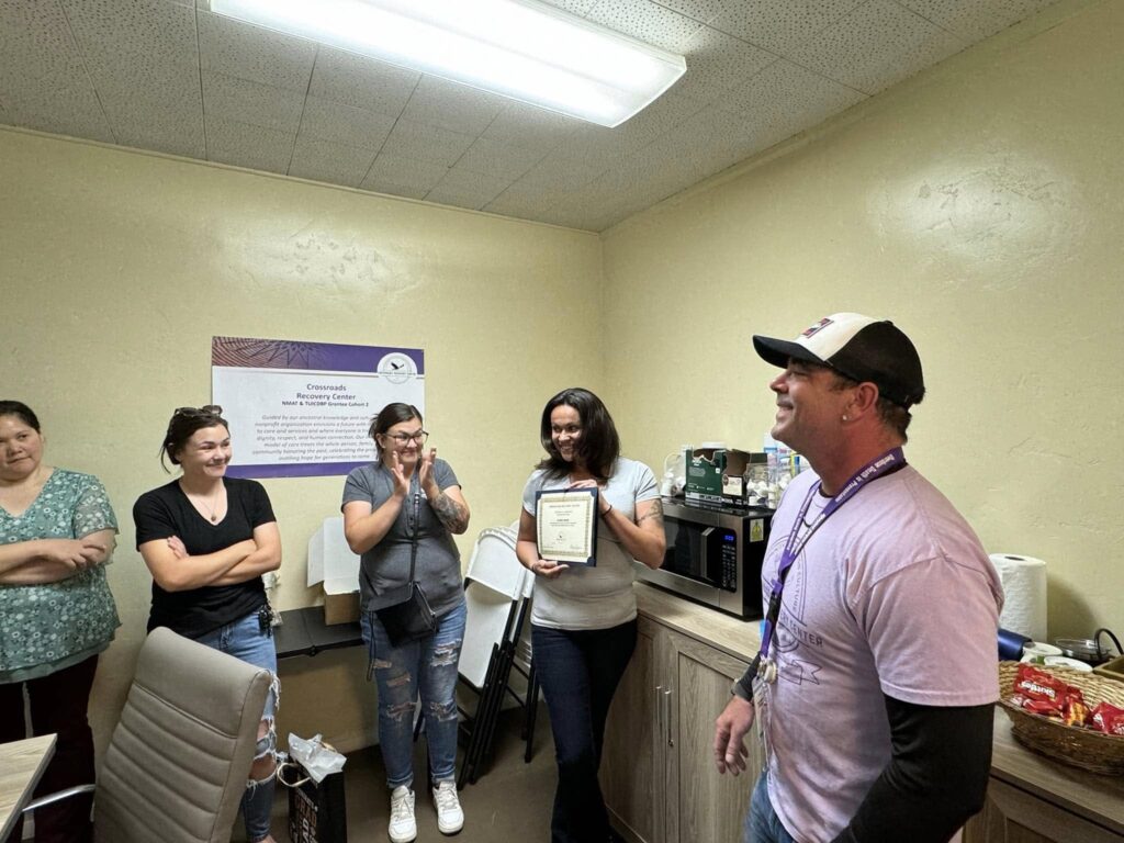 A group of people smiling and clapping as a woman shows off her certificate