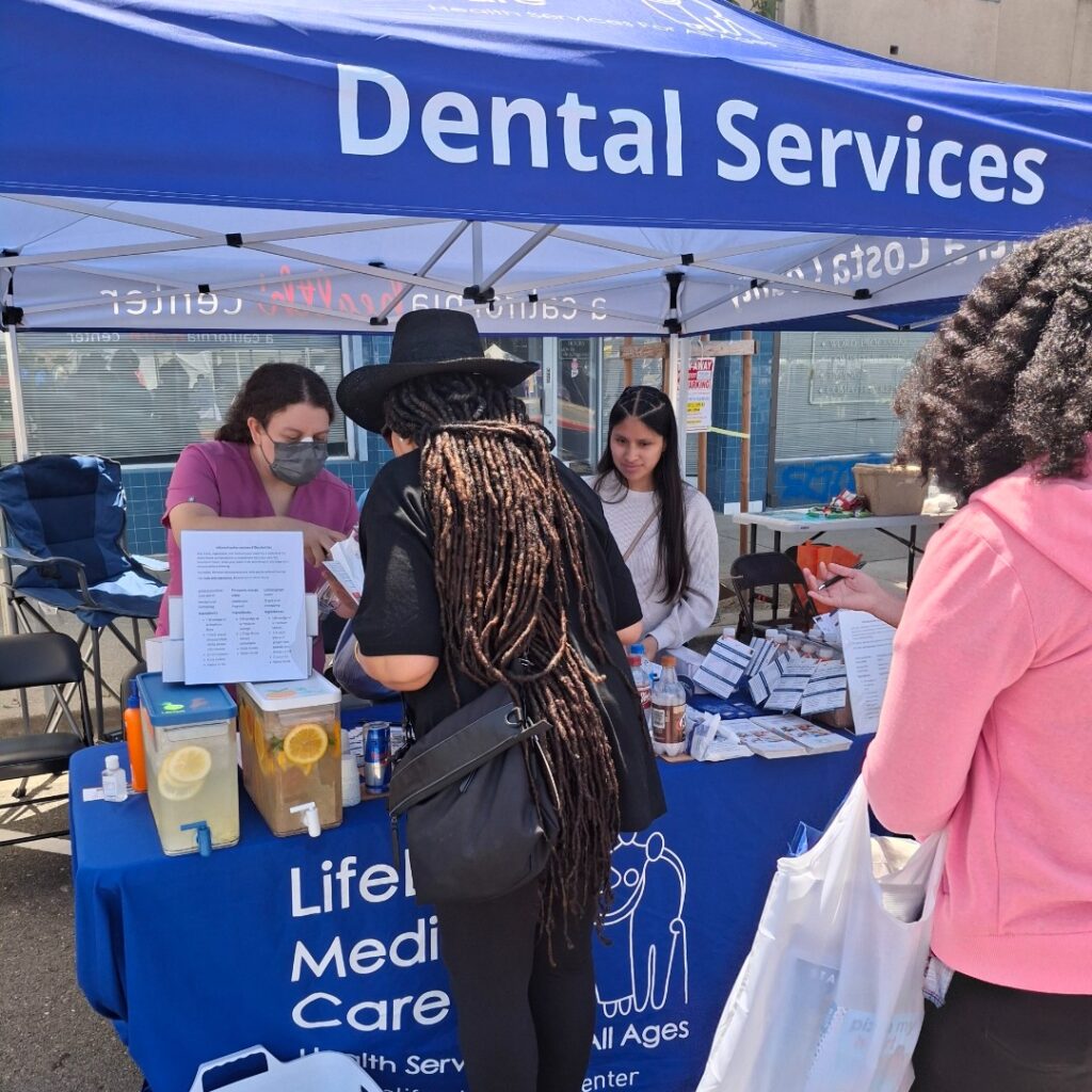 Two woman helping people at a Lifelong Medical Care dental services booth