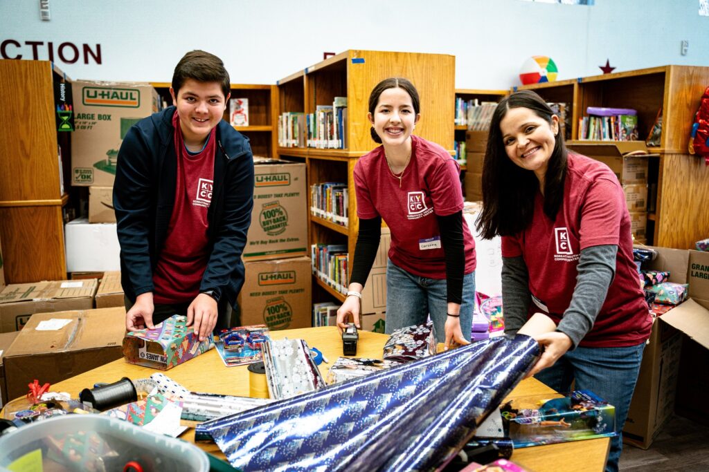 Three people with Koreatown Youth and Community Center (KYCC) shirts wrapping presents