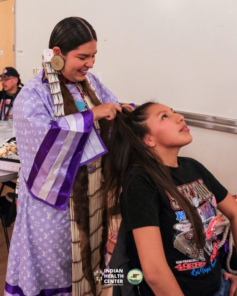Young woman in ceremonial garb braiding the hair of another young woman