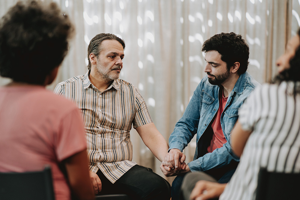 Man taking another man's hand in a support group circle