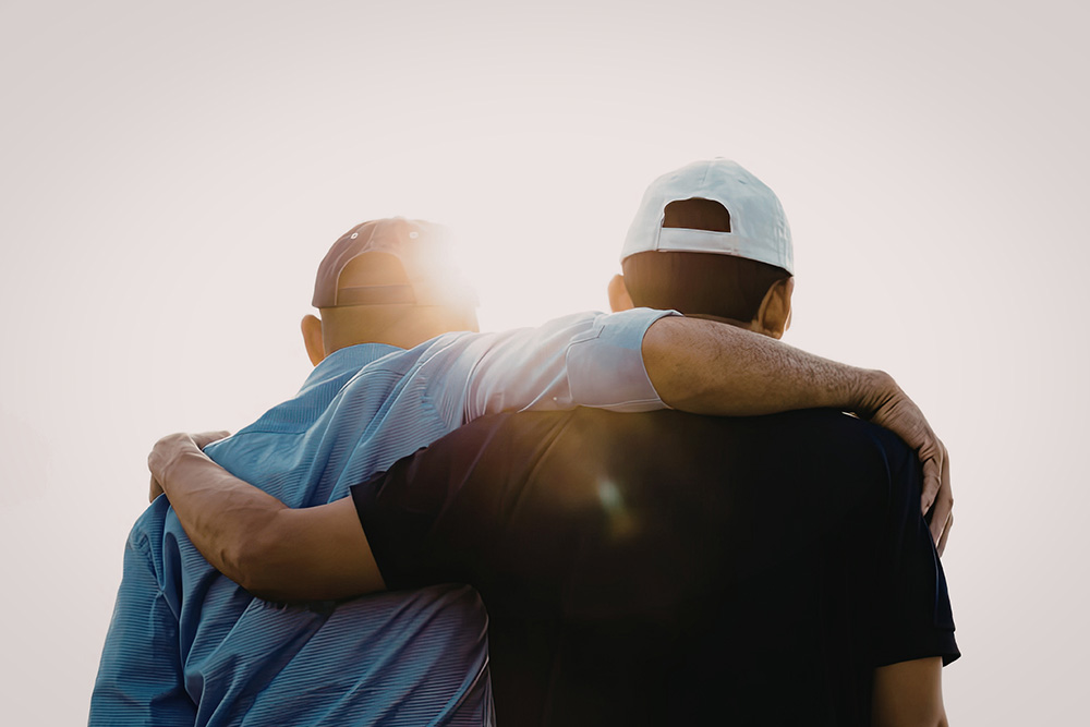 Two men arm in arm facing a bright sun