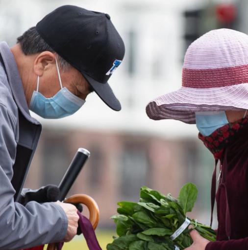 Asian-American couple wearing masks looking down at produce