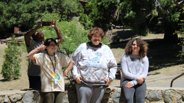 Three young people standing outside in front of a short stone wall