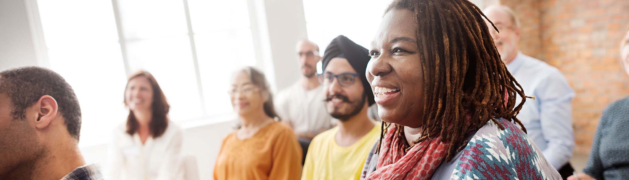 A diverse group of people smiling attentively in a sunlit room
