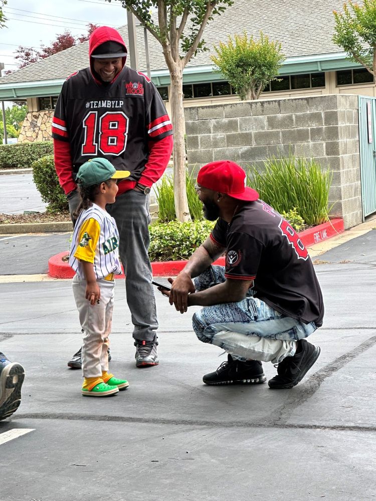 2 men with BYLP jerseys smiling with a little boy in a baseball uniform