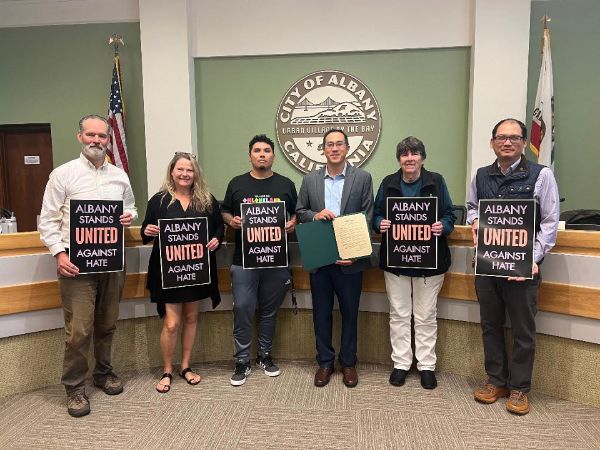 Six people in a Albany  government building holding united against hate posters